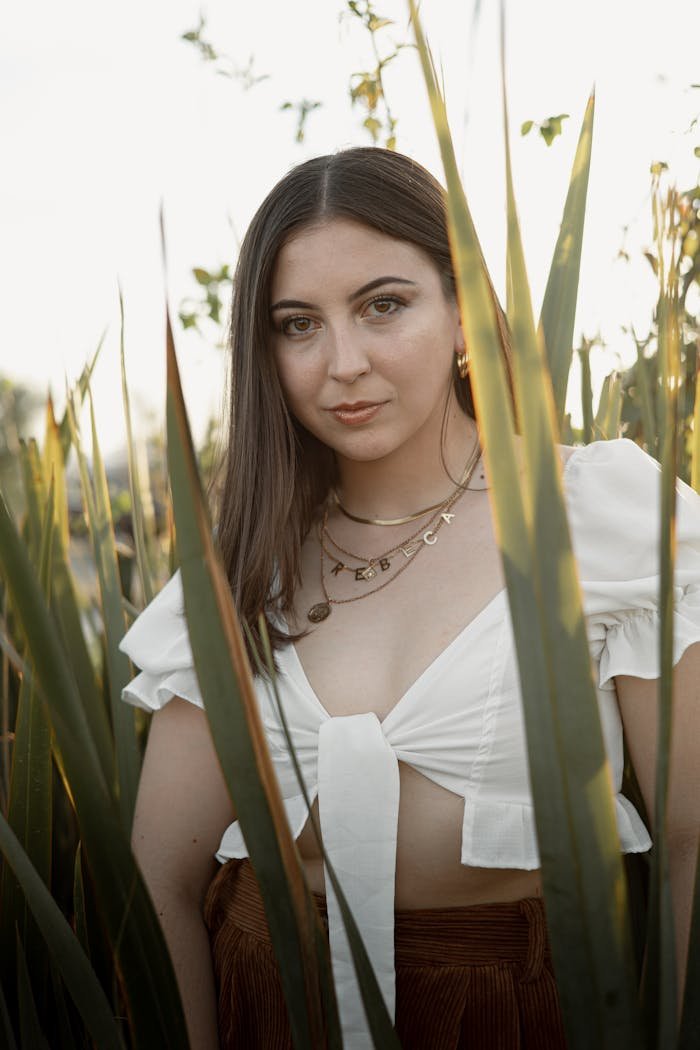 Portrait of a woman in a white top surrounded by tall grass and warm sunset light.