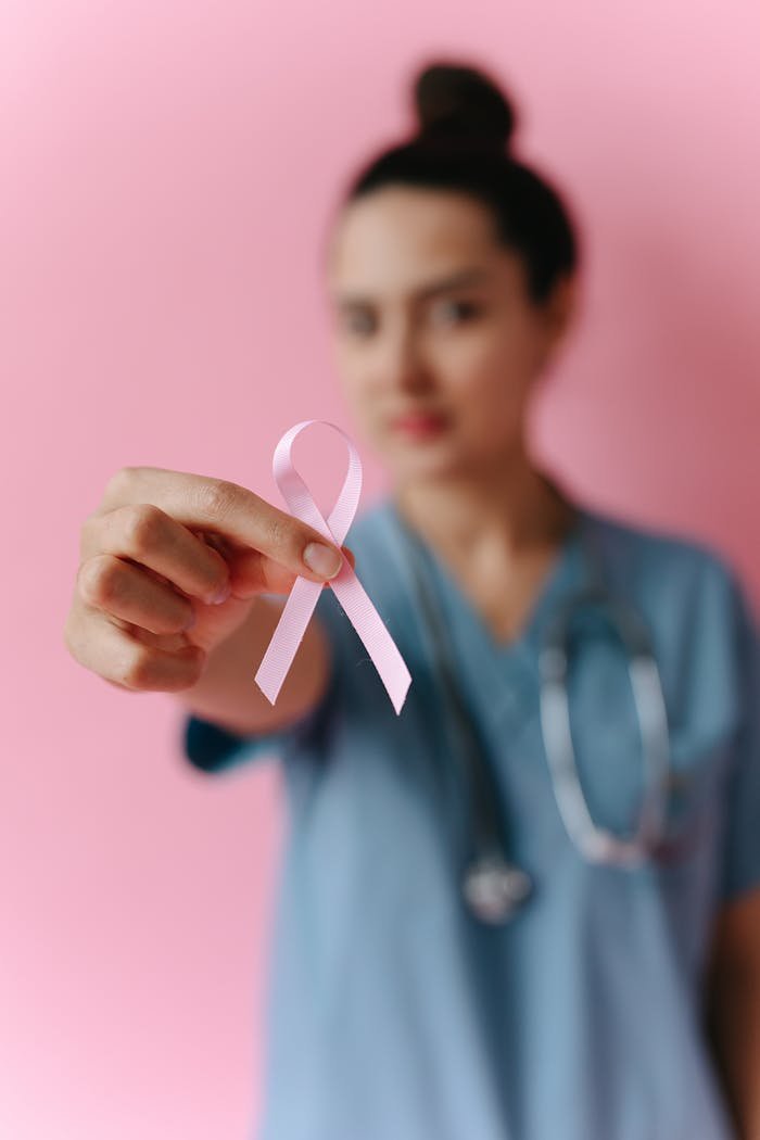 Healthcare worker holding a pink ribbon symbolizing breast cancer awareness against pink background.