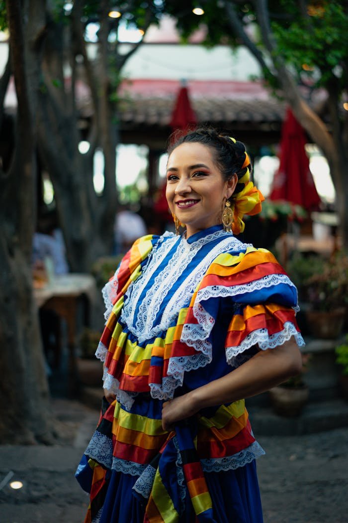 Smiling woman in traditional Mexican dress, celebrating culture outdoors.